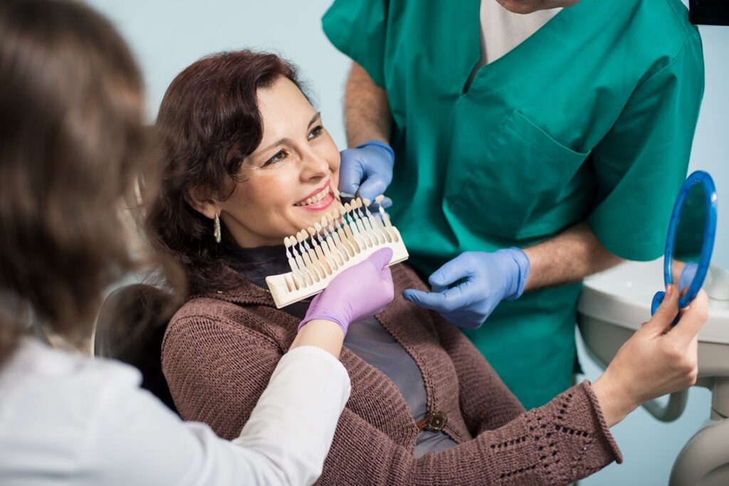 Faccette dentali e apparecchio (o allineatori trasparenti) le differenze - una donna dal dentista che guarda il suo sorriso allo specchio provando le faccette dentali